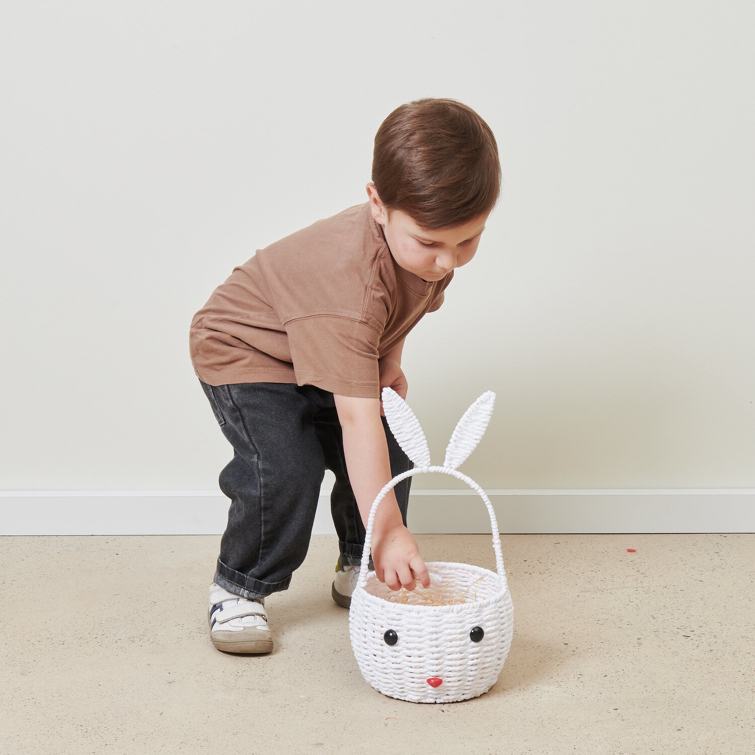 Osterkorb Hase: Kind in braunem Shirt greift nach weißem Korb mit Hasenohren von Rico Design.
