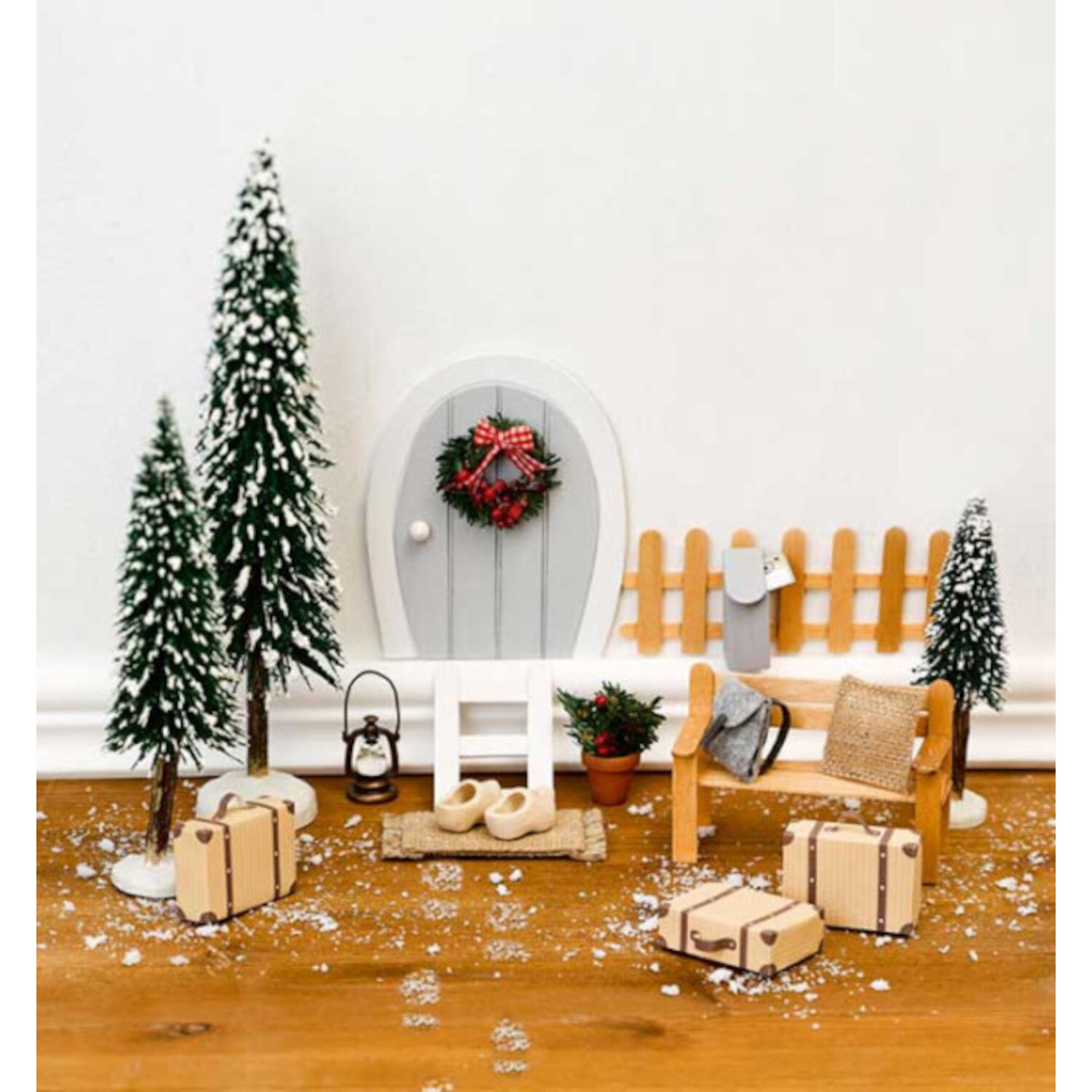 Weihnachtliche Wichteltüren: Miniatur-Szene mit verschneiten Tannen, Geschenken und einer grauen Tür. Ideal für festliche Dekorationen.