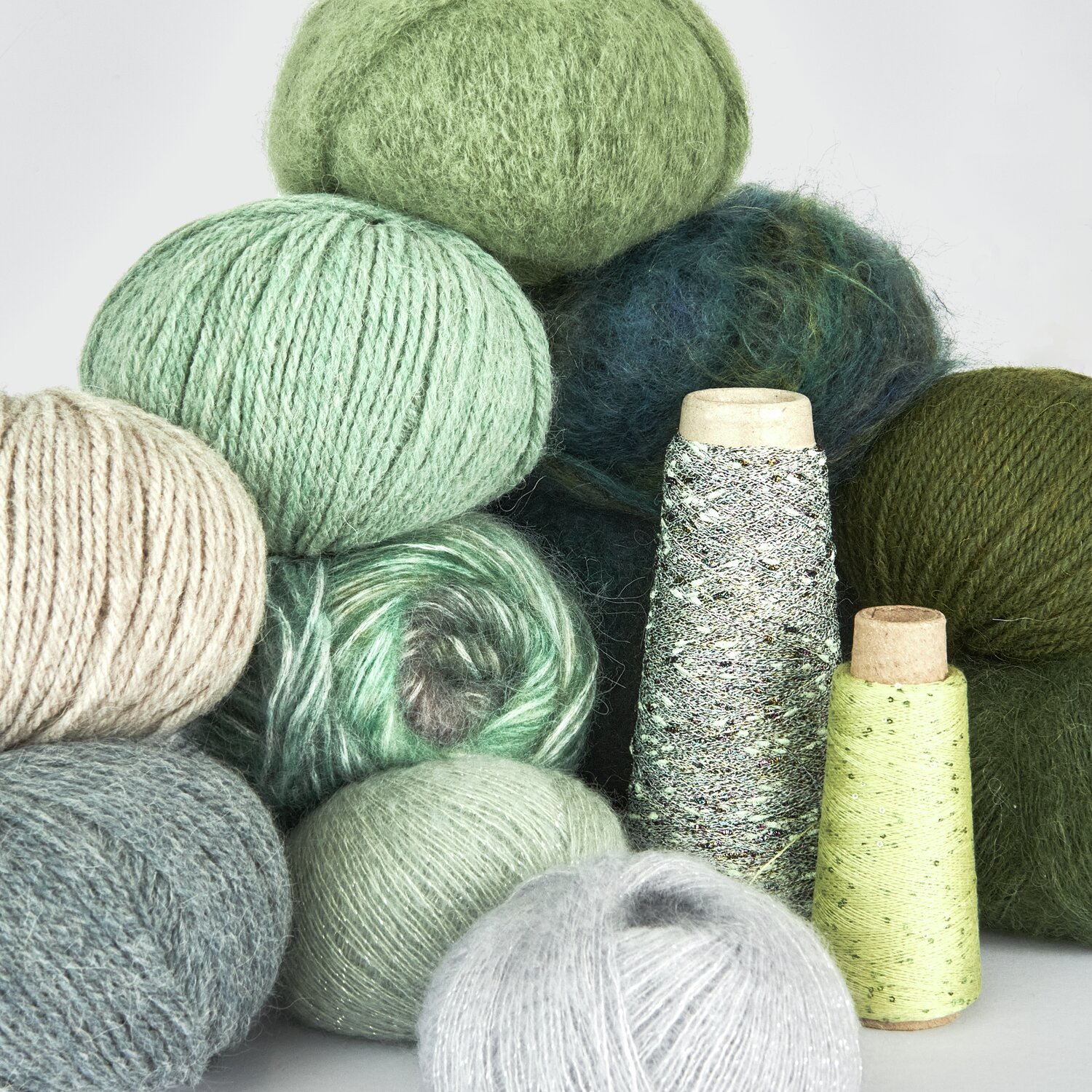 Lovewool No. 21 Herbst-Winter Sprachauswahl deutsch von Rico Design Verschiedene Wollknäuel und Garnspulen in Grün- und Grautönen, ideal für Strick- und Häkelprojekte. Die Texturen variieren von flauschig bis glatt, perfekt für kreative Handarbeiten.