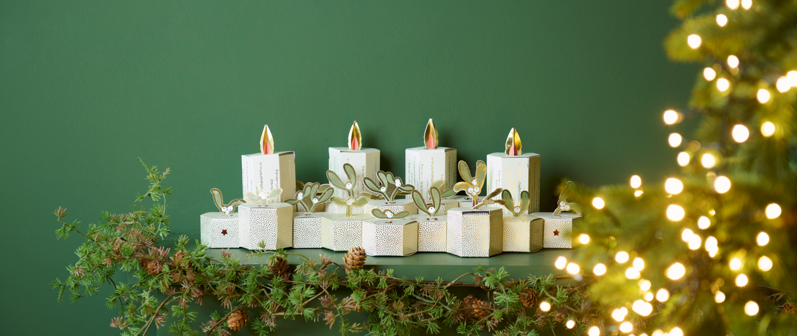 Adventskalender in  Kerzenformaus Papier mit Tannenzweigen und Lichterdekoration auf einem Regal.