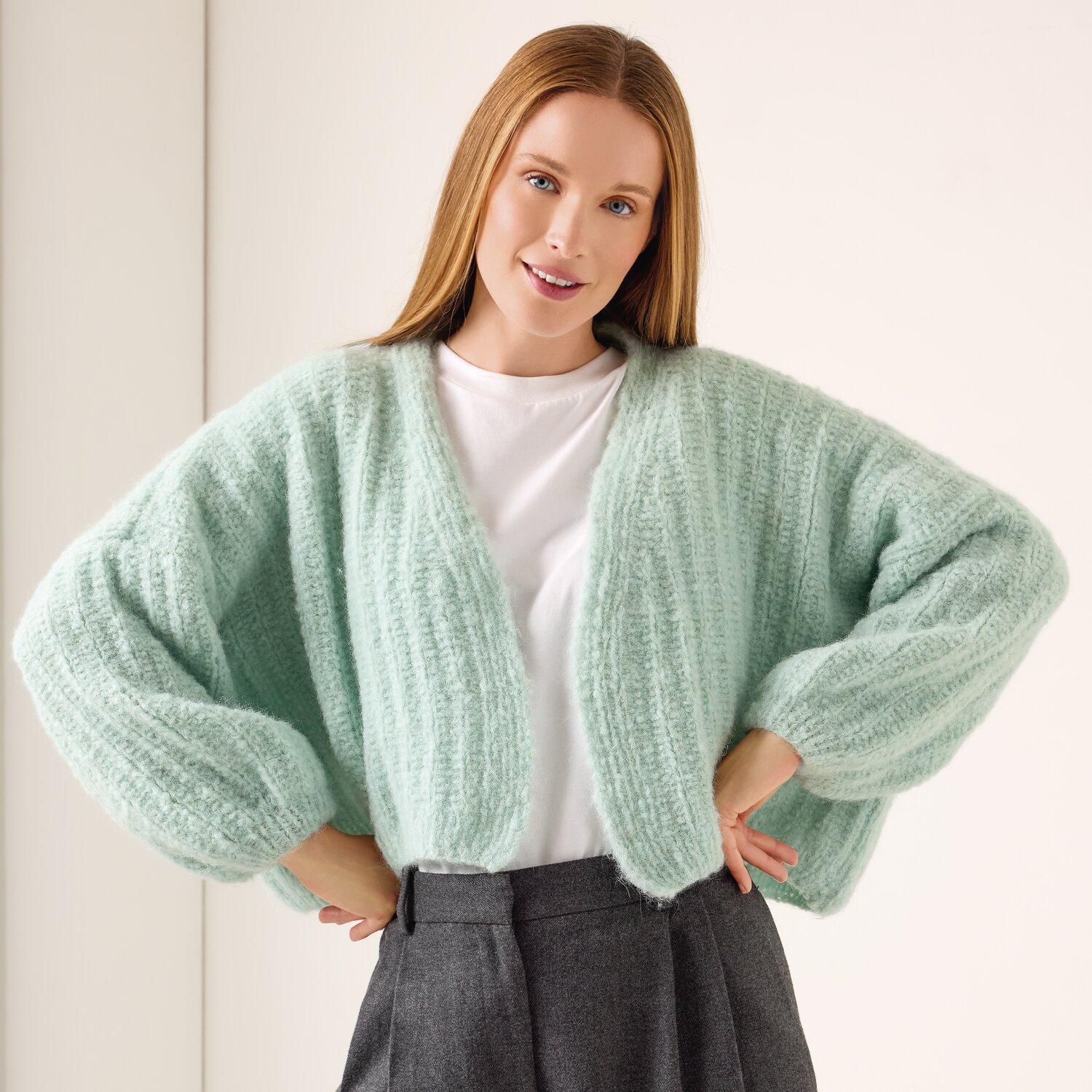 Strickset Jacke Modell 23 aus Die Neue Masche No. 13 von idee. Creativmarkt Strickset Jacke Modell 23 aus Die Neue Masche No. 13: Frau trägt mintgrüne Strickjacke über weißem Shirt, kombiniert mit grauer Hose.