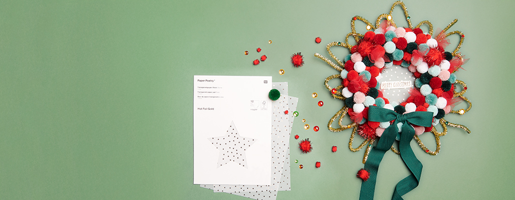 Ein weihnachtlicher Türkranz bestehend aus roten und grünen Pompons mit einer Schleife und Transparentpapier verziert. Fotosetting grüner Hintergrund.