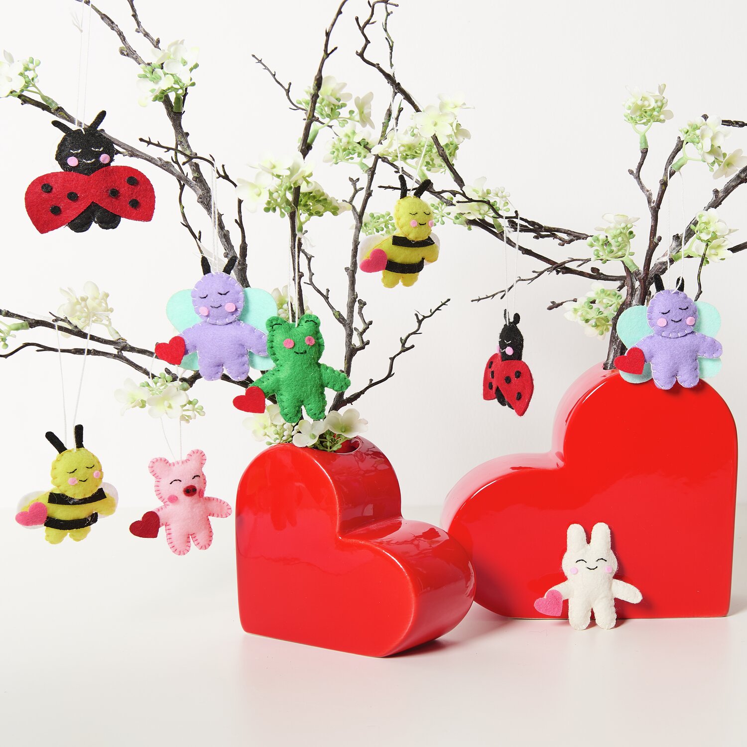 Aufhänger Filz-Hase 2D Weiß: Bunte Filzfiguren an Zweigen, dekoriert mit roten Herzboxen. Ideal für kreative Dekorationen.