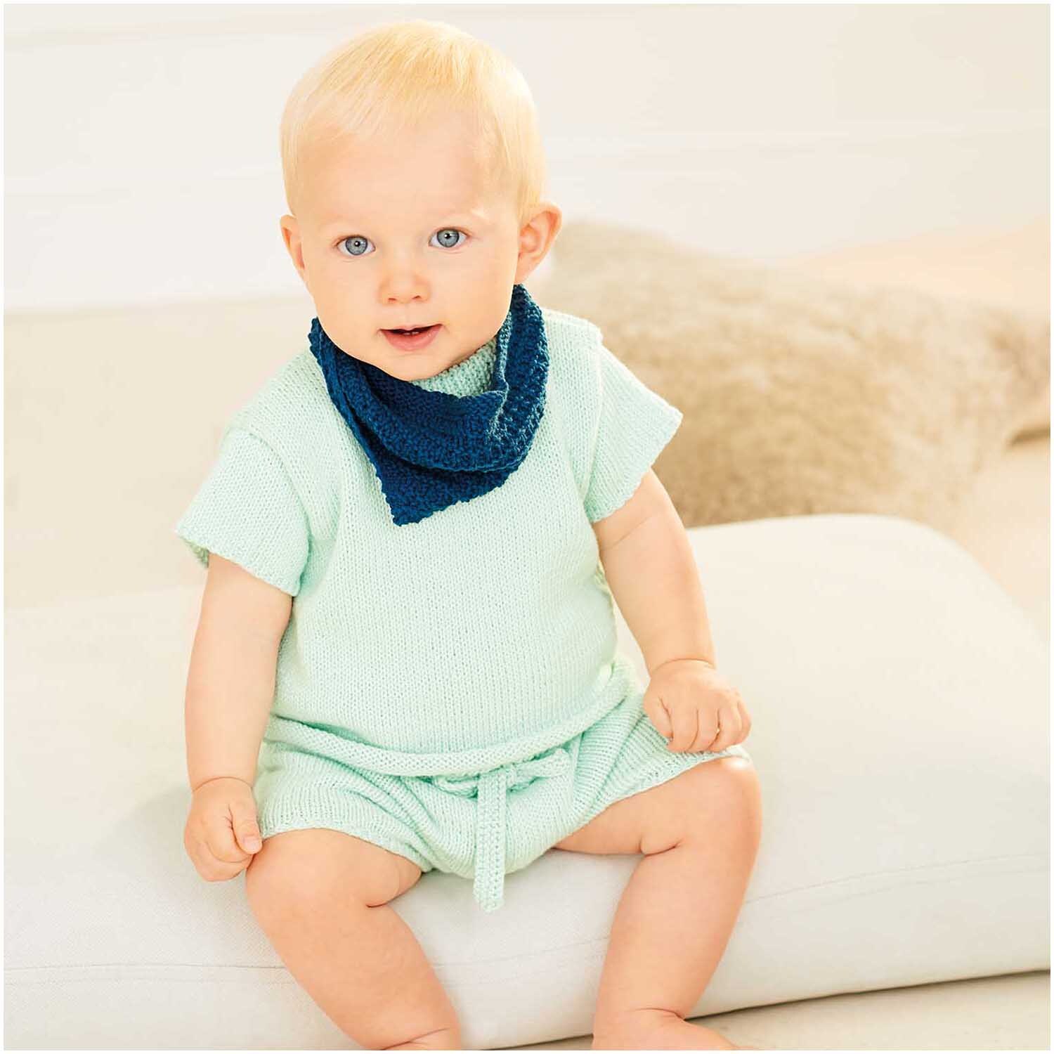 Baby Organic Cotton 50g 150m Farbe Marine von Rico Design Baby Organic Cotton: Ein Baby trägt ein mintgrünes Outfit mit marineblauem Halstuch, sitzt auf einem weißen Kissen.