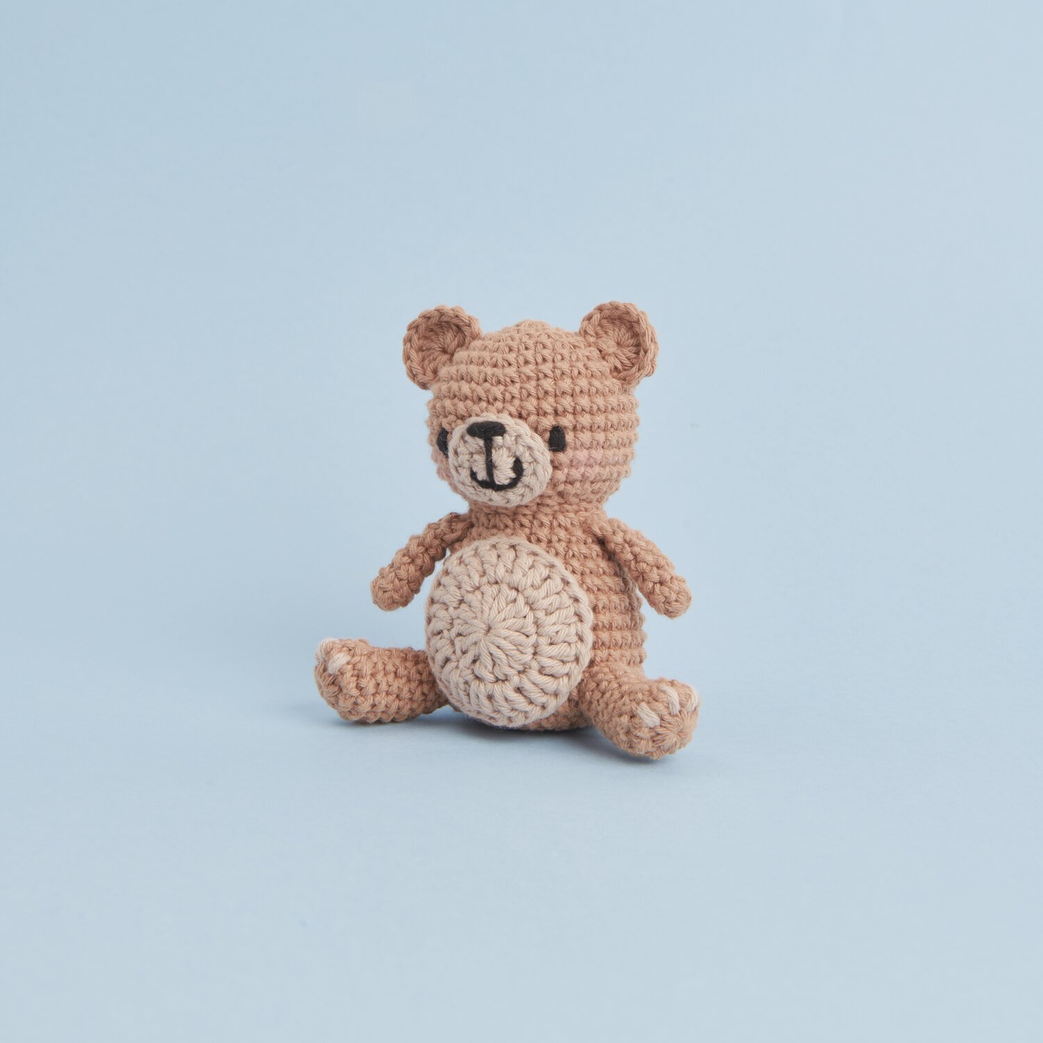 Ricorumi Mini Easy Häkelset - Teddy: Niedlicher gehäkelter Bär in Beige von Rico Design vor blauem Hintergrund.