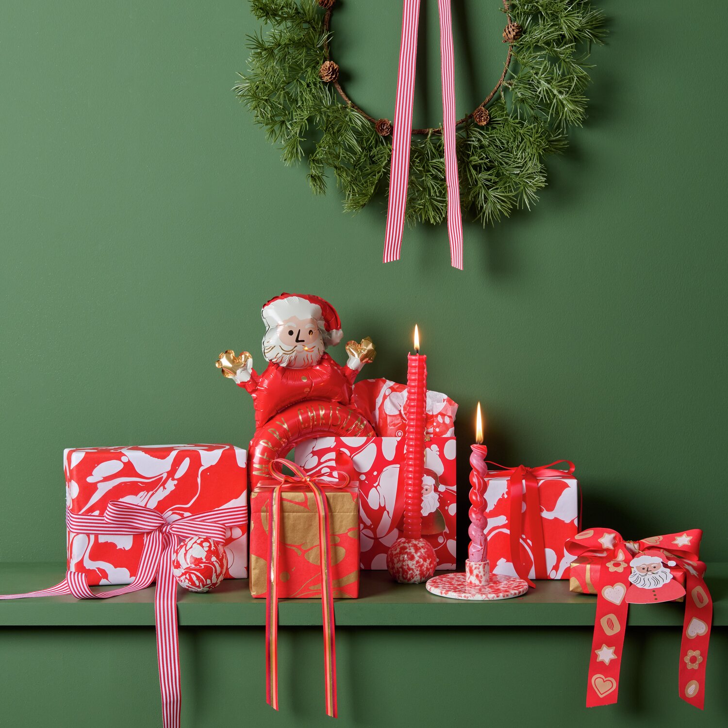 Ein festlich dekoriertes Regal mit einem roten und weißen Porzellan-Kerzenhalter von Rico Design. Umgeben von Geschenken und Dekorationen in Rot und Weiß, ideal für weihnachtliche Stimmung.