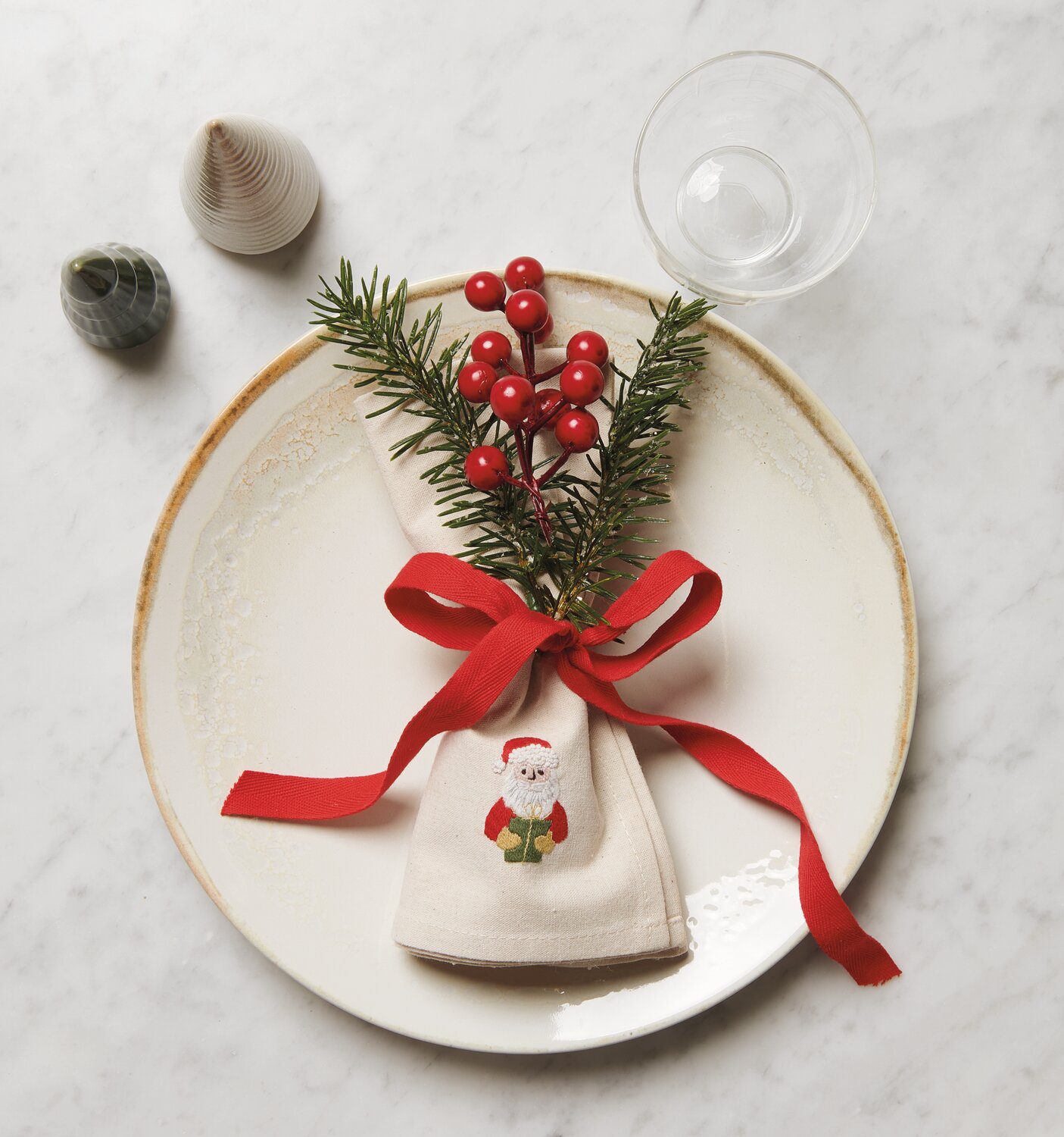 Stick & Stitch Stickpackung Weihnachtsmann zeigt ein festliches Tischset mit rotem Band und Tannenzweigen.