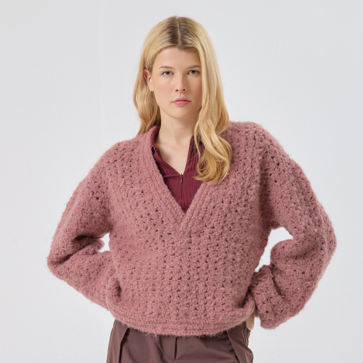 Häkelset Pullover Modell 36 aus Made by Me No. 21 von Rico Design Häkelset Pullover Modell 36 aus Made by Me No. 21: Frau trägt rosa V-Pullover, kombiniert mit bordeauxroter Bluse und brauner Hose.