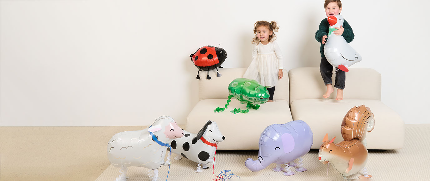 Zwei Kinder stehen auf einem Sofa mit vielen Folienballons in Tierform aus der Kollektion Rico Chingus.