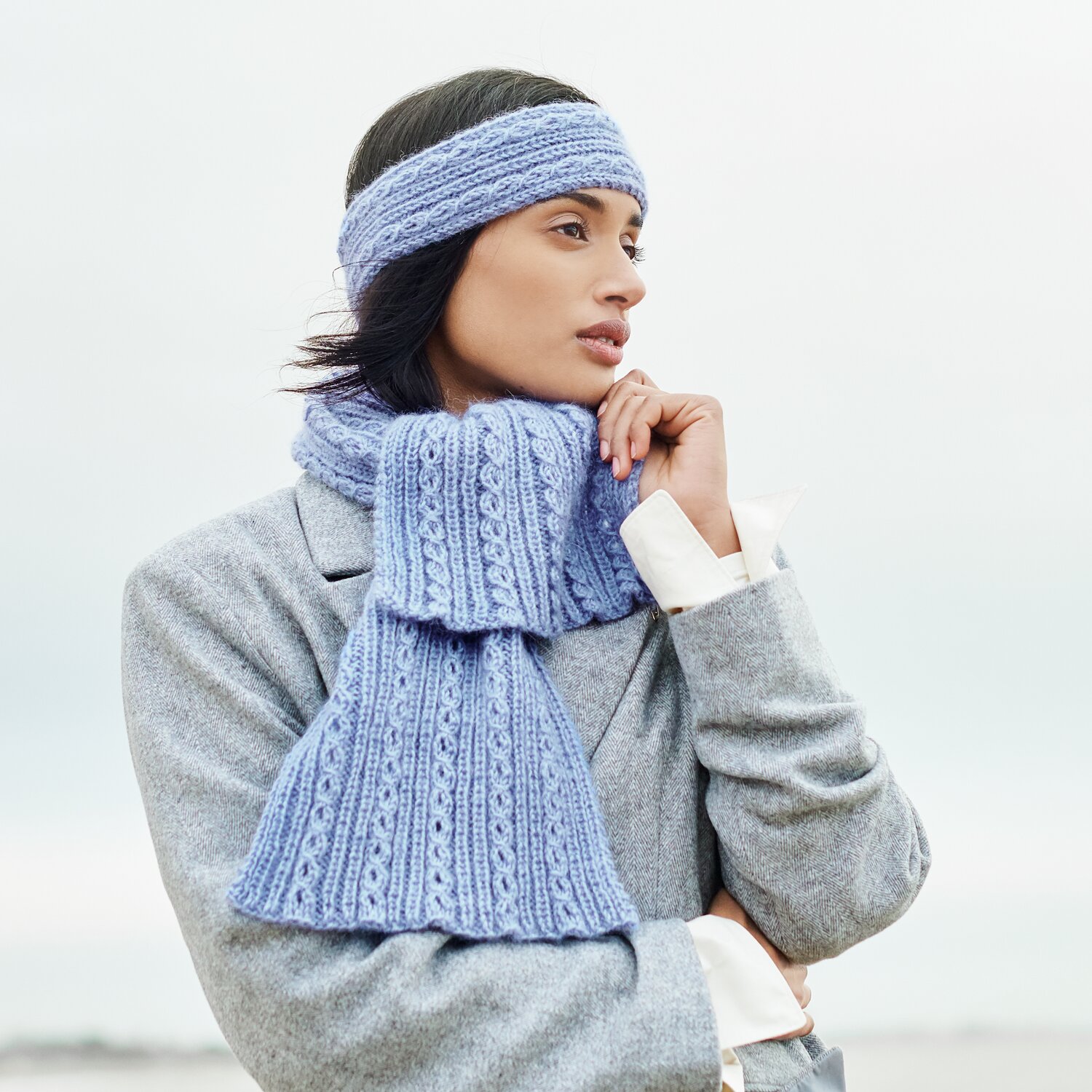 Strickset Stirnband Modell 30 aus Lovewool No. 21 von Rico Design Strickset Schal Modell 29 aus Lovewool No. 21: Frau trägt blauen Schal und Stirnband, stilvoll kombiniert mit grauem Mantel.