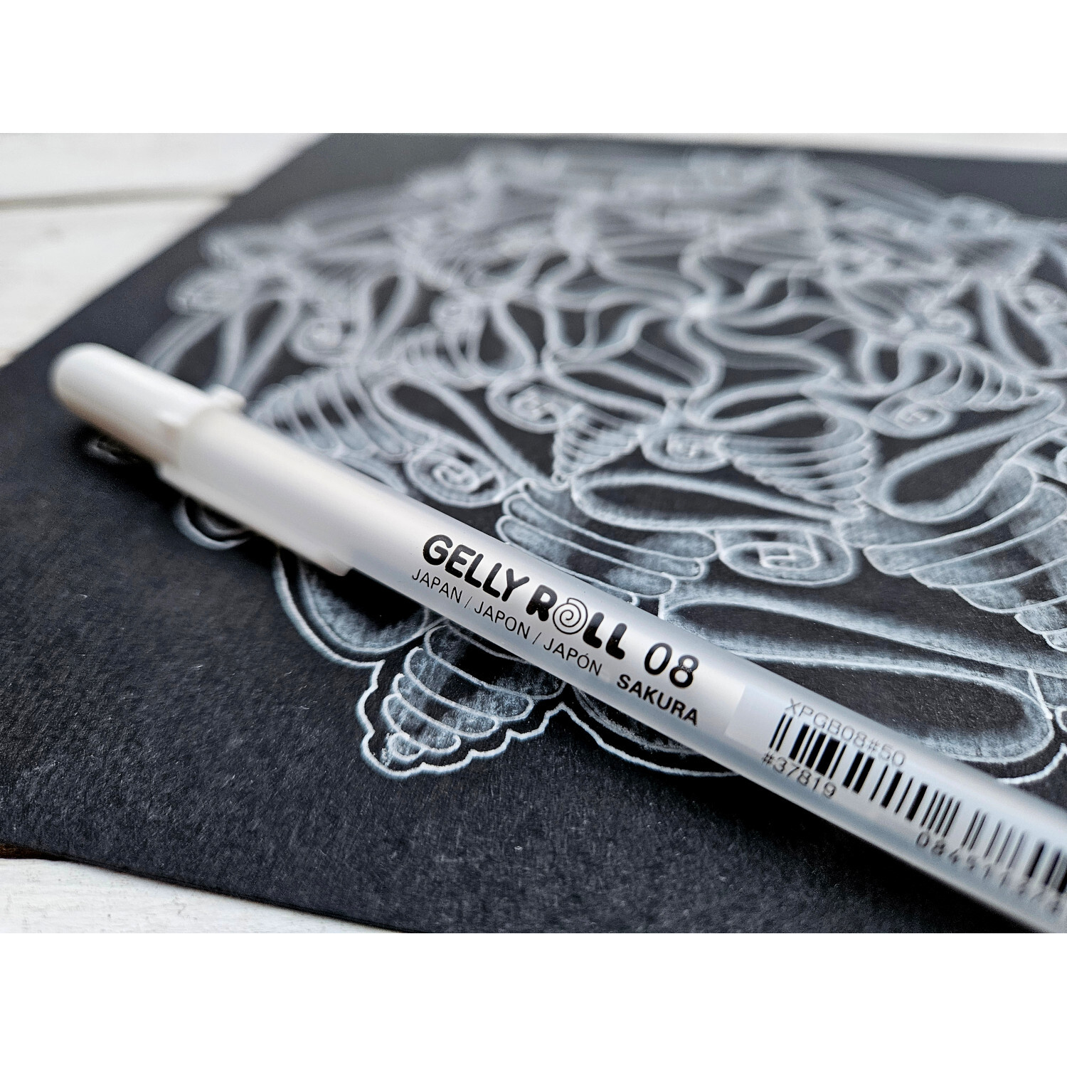 Gelly Roll Basic Gelstift weiß von SAKURA auf schwarzem Papier mit detailliertem Muster.