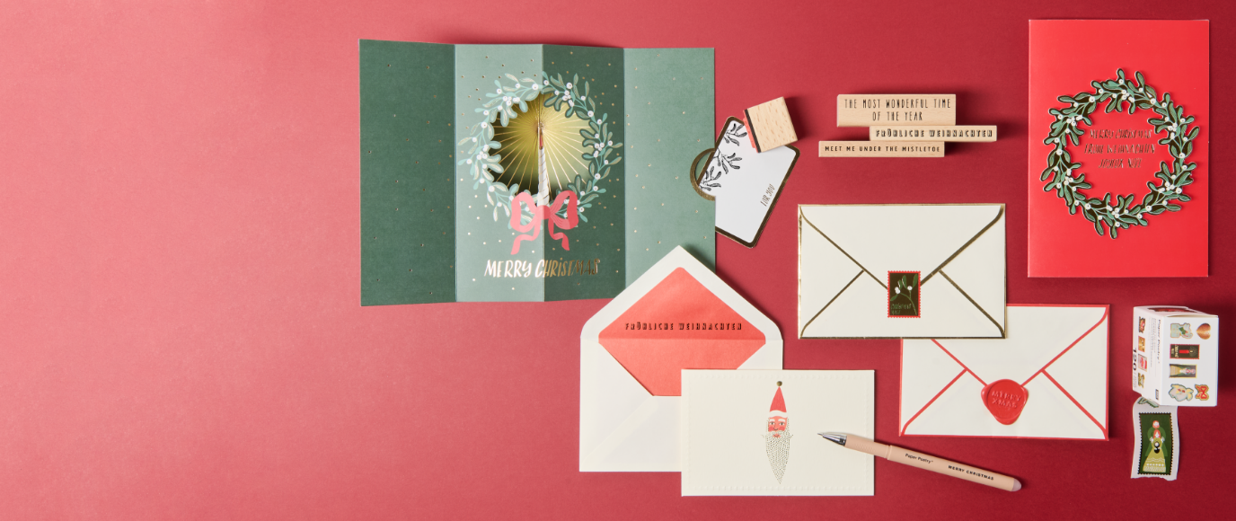 Selbstgestaltete Weihnachtskarten mit Stempeln und Briefpapier auf rotem Hintergrund.