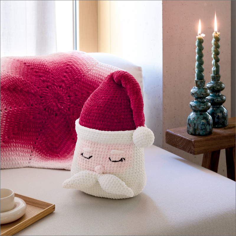 Gehäkeltes Weihnachtskissen im Nikolaus-Design auf einem Sofa.