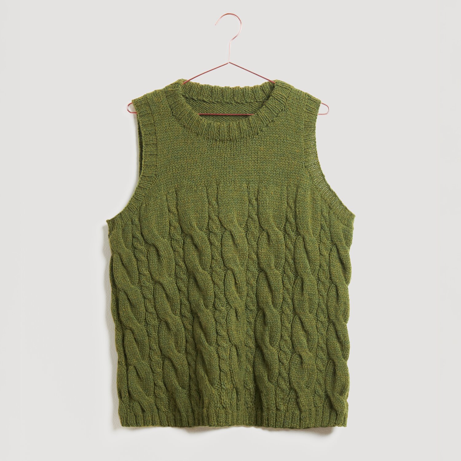 Lovewool No. 21 Herbst-Winter Sprachauswahl deutsch von Rico Design Ärmelloser, olivgrüner Strickpullover mit Zopfmuster, aufgehängt an einem Kleiderbügel. Marke: Modell Legeware. Perfekt für einen stilvollen, lässigen Look.