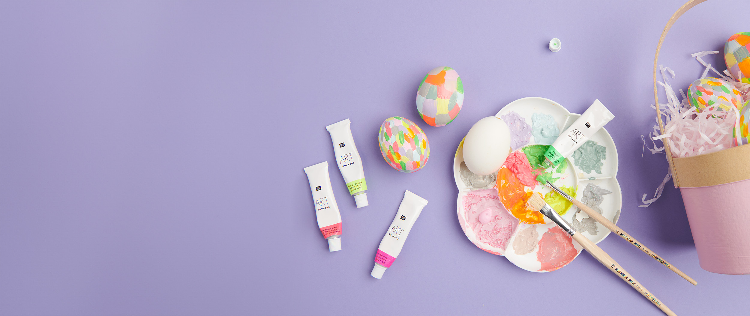Weiße Eier werden mit Acrylfarben bunt bemalt, Farbpalette und Osterkörbchen sind zu sehen