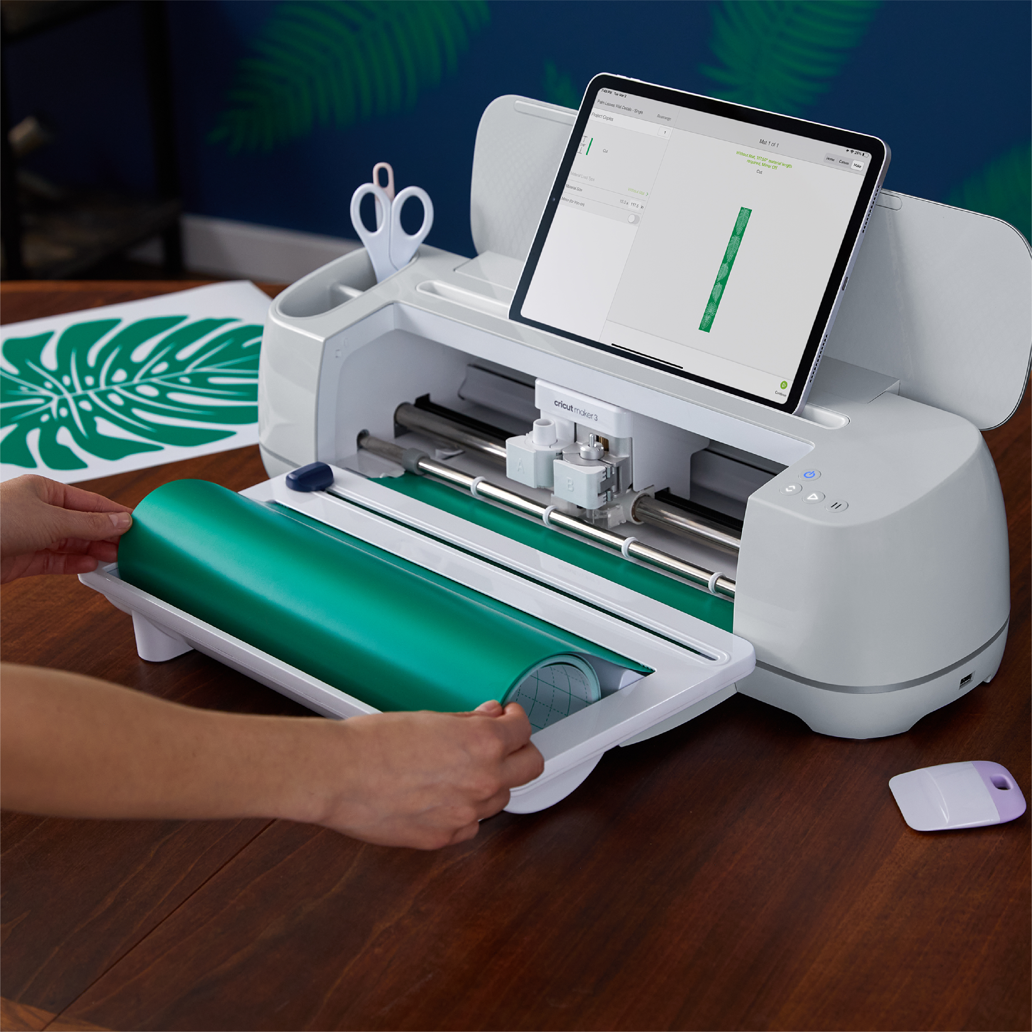 Ein großer Schneideplotter wird mit grünem Papier und von Händen bedient.