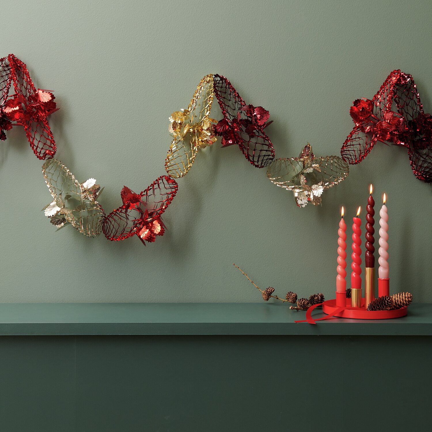 Foliengirlande in Rot und Gold von Rico Design, 2,3m lang, dekoriert mit Kerzen auf einem Regal.