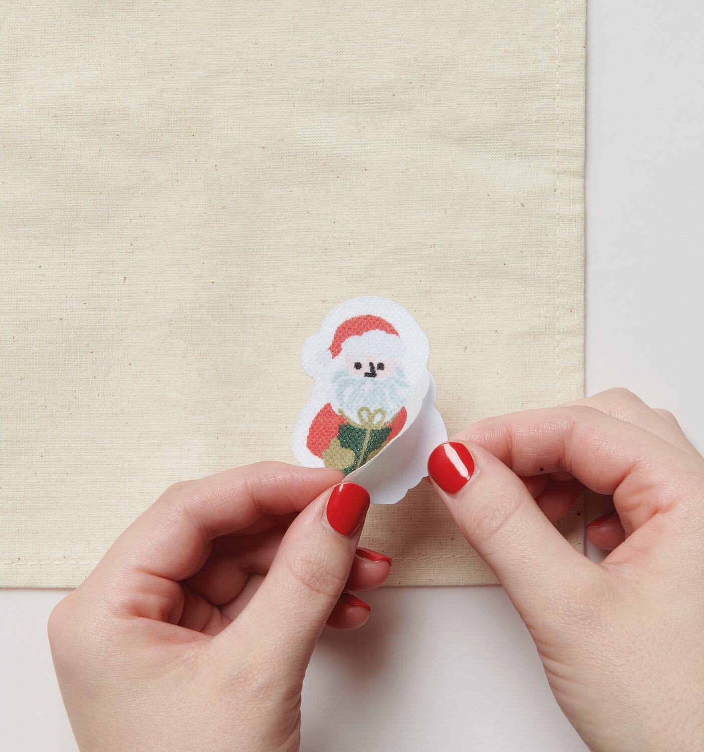 Stick & Stitch Stickpackung Weihnachtsmann 13 Stück: Hände platzieren Aufkleber auf beigem Stoff.