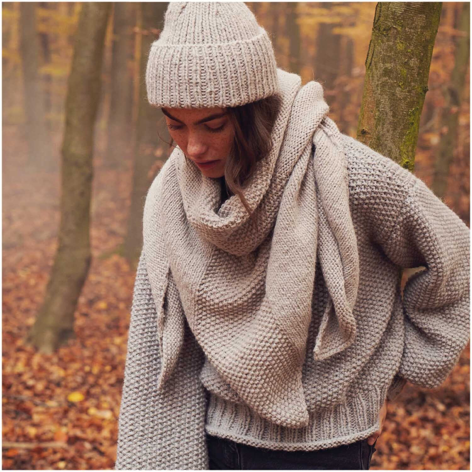 Essentials Alpaca Twist Chunky: Frau in gestricktem Schal und Mütze im herbstlichen Wald.