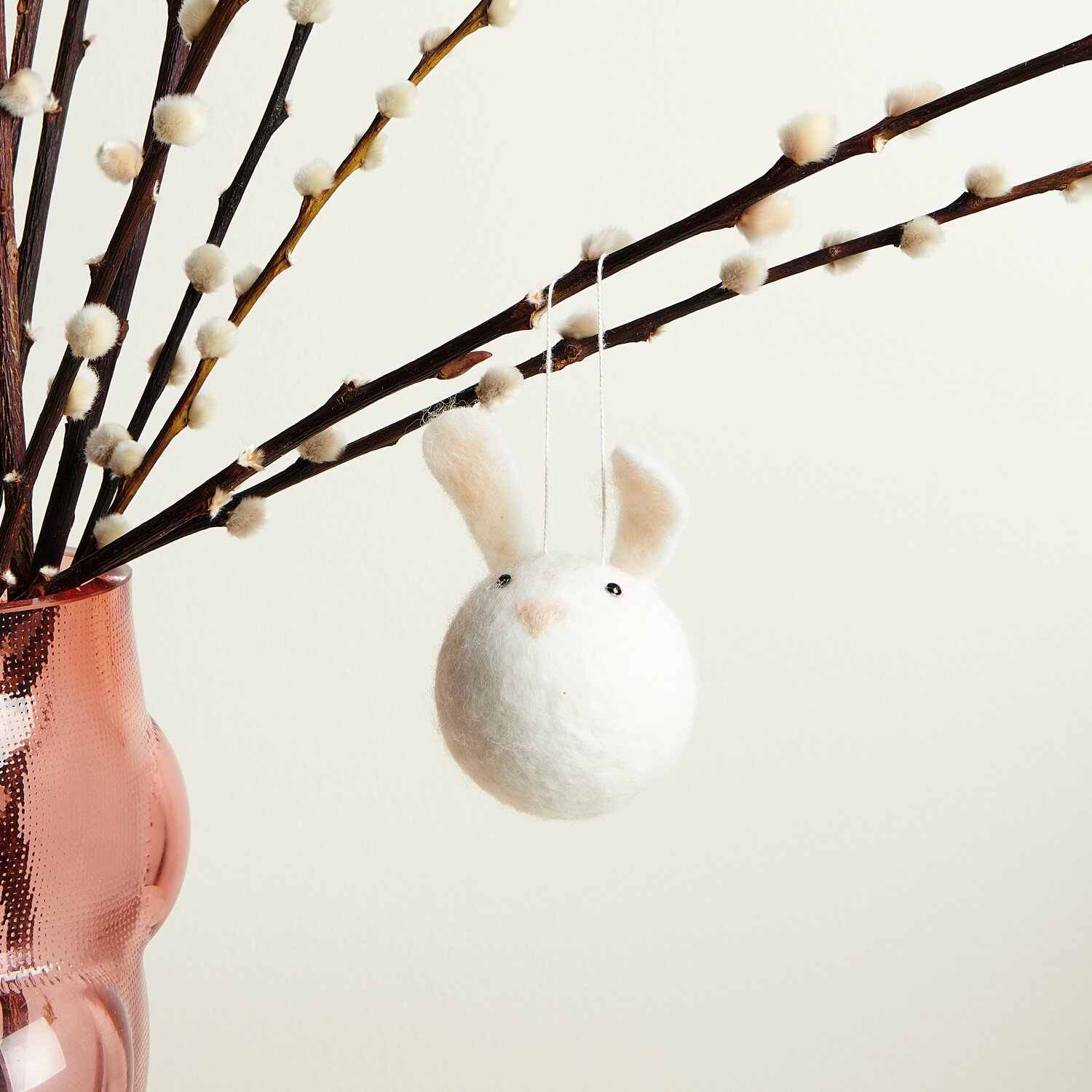 Aufhänger Filz-Hasenkopf Weiß: Niedlicher Hasenkopf aus Filz an einem Ast, dekorativ in einem rosa Glasgefäß arrangiert.