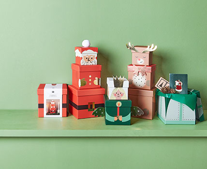 Geschenkschachteln jeweils so übereinandergestapelt, dass sie einen Weihnachtsmann, ein Rentier und einen Engel darstellen. Fotosetting grüne Wand.