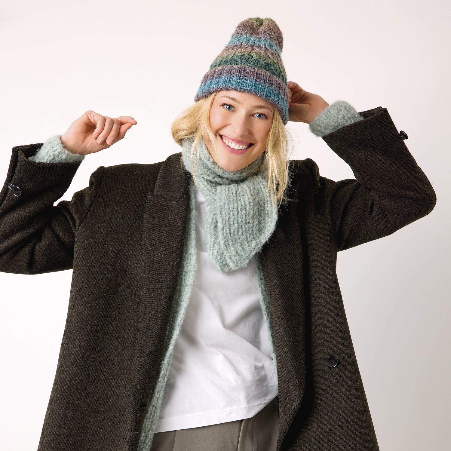 Strickset Schal Modell 26 aus Die Neue Masche No. 13 von idee. Creativmarkt Strickset Schal Modell 26: Frau trägt mintgrünen Schal und Mütze, brauner Mantel, lächelnd.