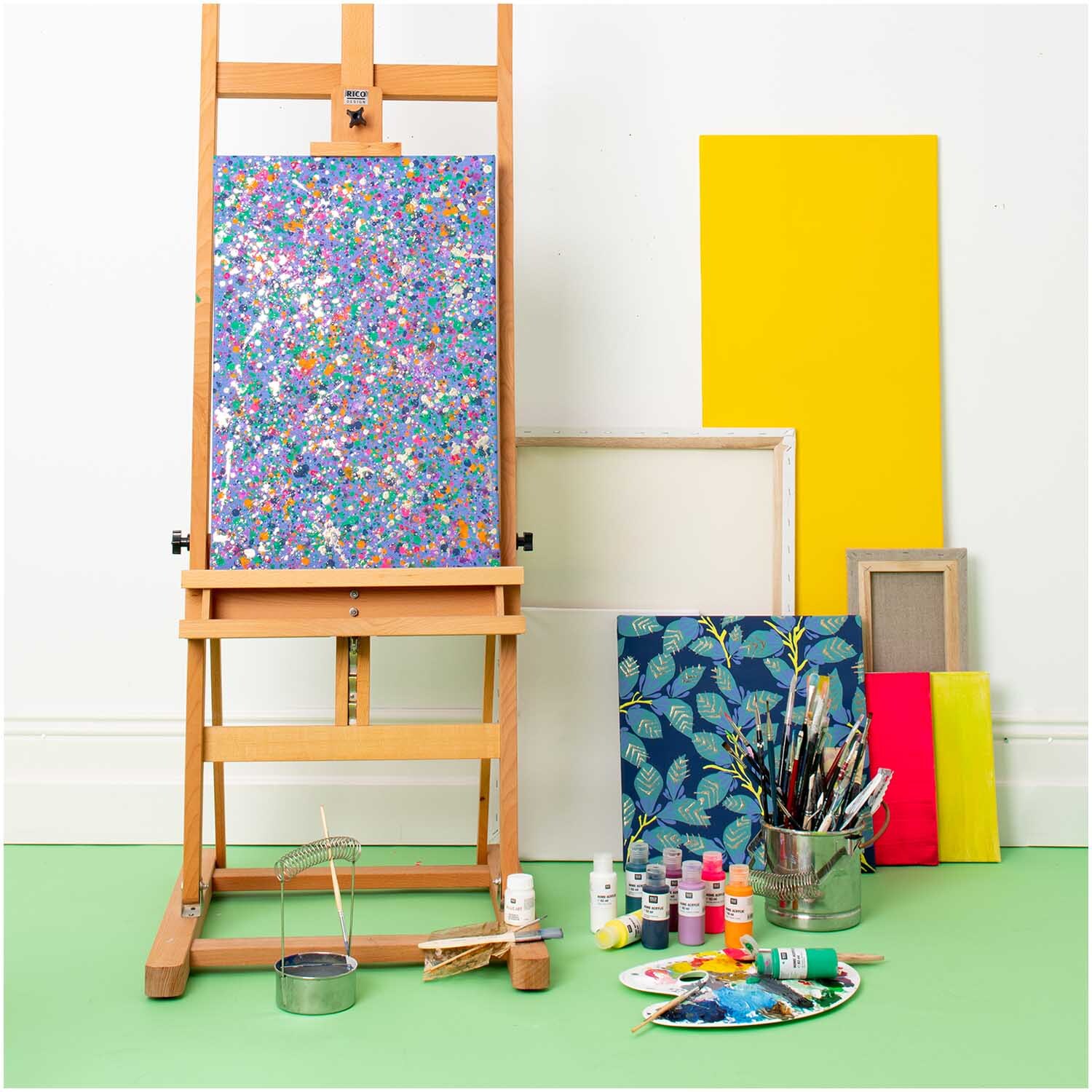 Home Acrylic  82ml Farbe Lavendel von Rico Design Home Acrylic: Bunte Malutensilien auf grünem Boden, Staffelei mit farbenfrohem Bild, gelbe Leinwand.