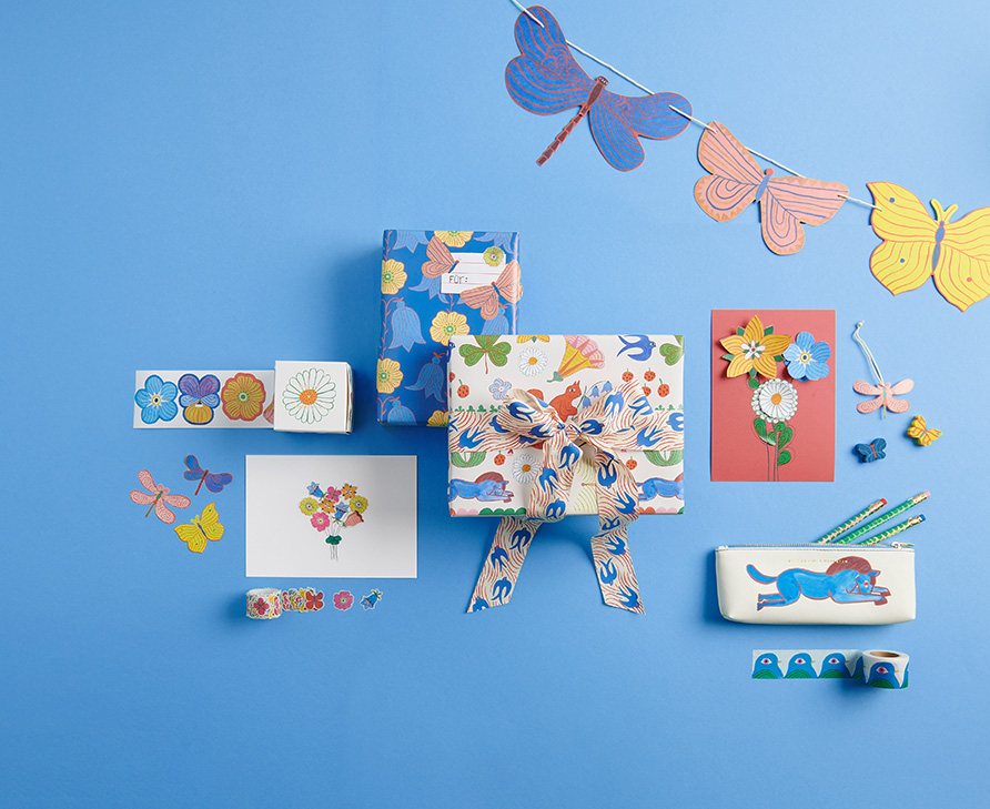 Geschenkpapier, eingepackte Geschenke, Blumensticker, Karten, Stifte in einem Etui und Girlande aus Schmetterlingen. Flatlay von Produkten.