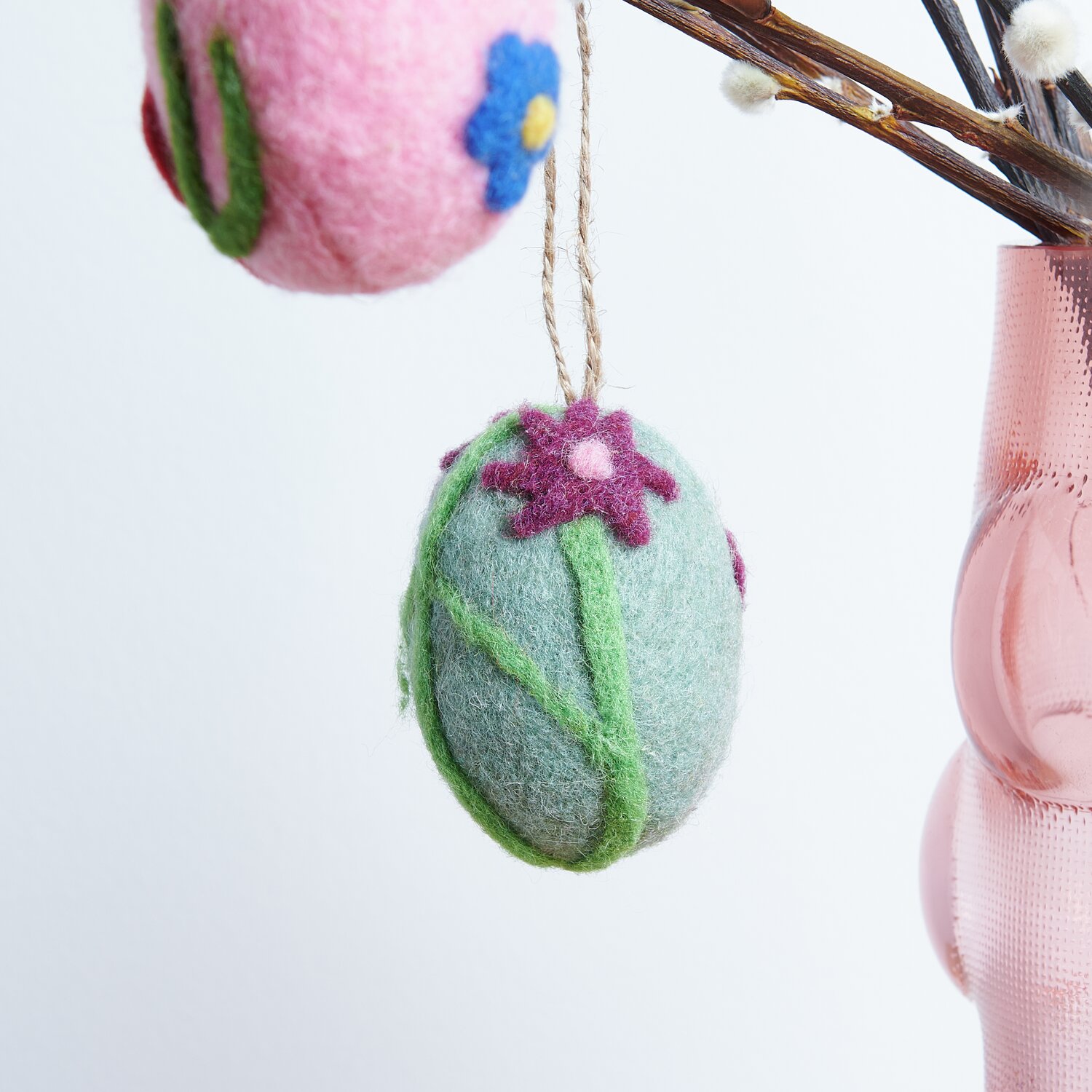 Aufhänger Filz-Ei Purpur-Blume: Dekoratives Filz-Ei mit Blumenmotiv in Rosa und Grün, ideal für Frühlingsdekorationen. Größe: 7,8xØ5,8cm.