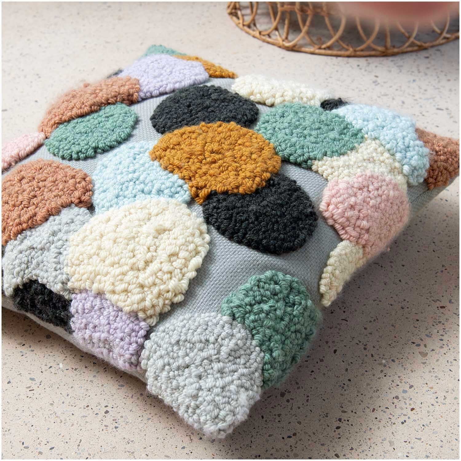 Punch Needle Packung Kissen Punkte bunt von Rico Design zeigt ein farbenfrohes Kissen mit runden, texturierten Mustern auf einem hellen Hintergrund.