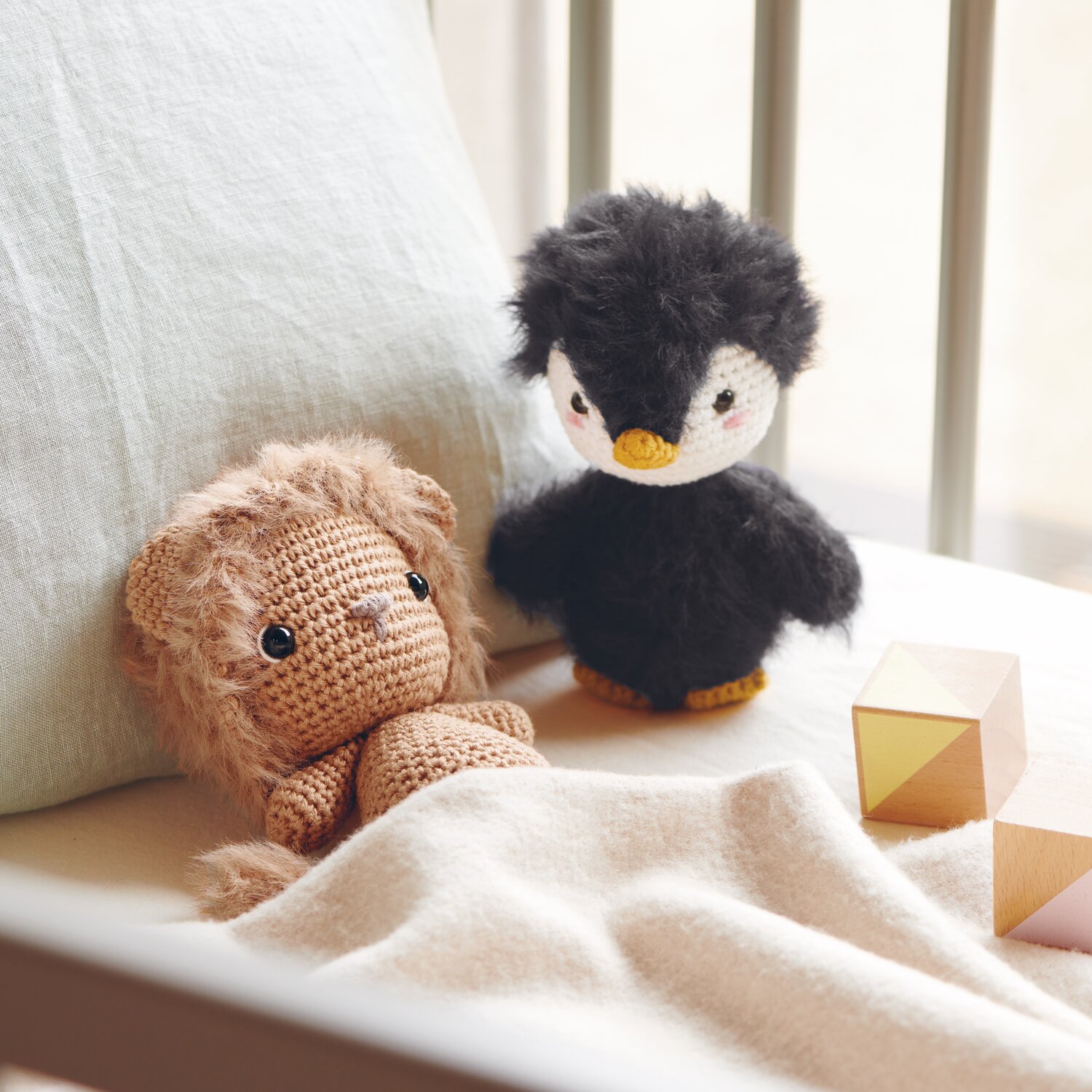 Creative Ricorumi dk 25g Farbe Schwarz von Rico Design Ricorumi Furry Animals: Kuscheltier-Löwe in Karamell und Pinguin in Schwarz auf Bett mit Holzklötzen.