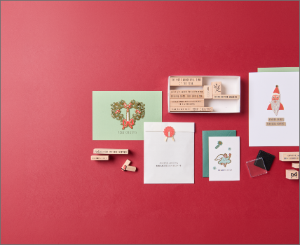 Weihnachtliches Bastelset mit Grußkarten, Stempeln, Holzbuchstaben und Bastelzubehör auf rotem Hintergrund.
