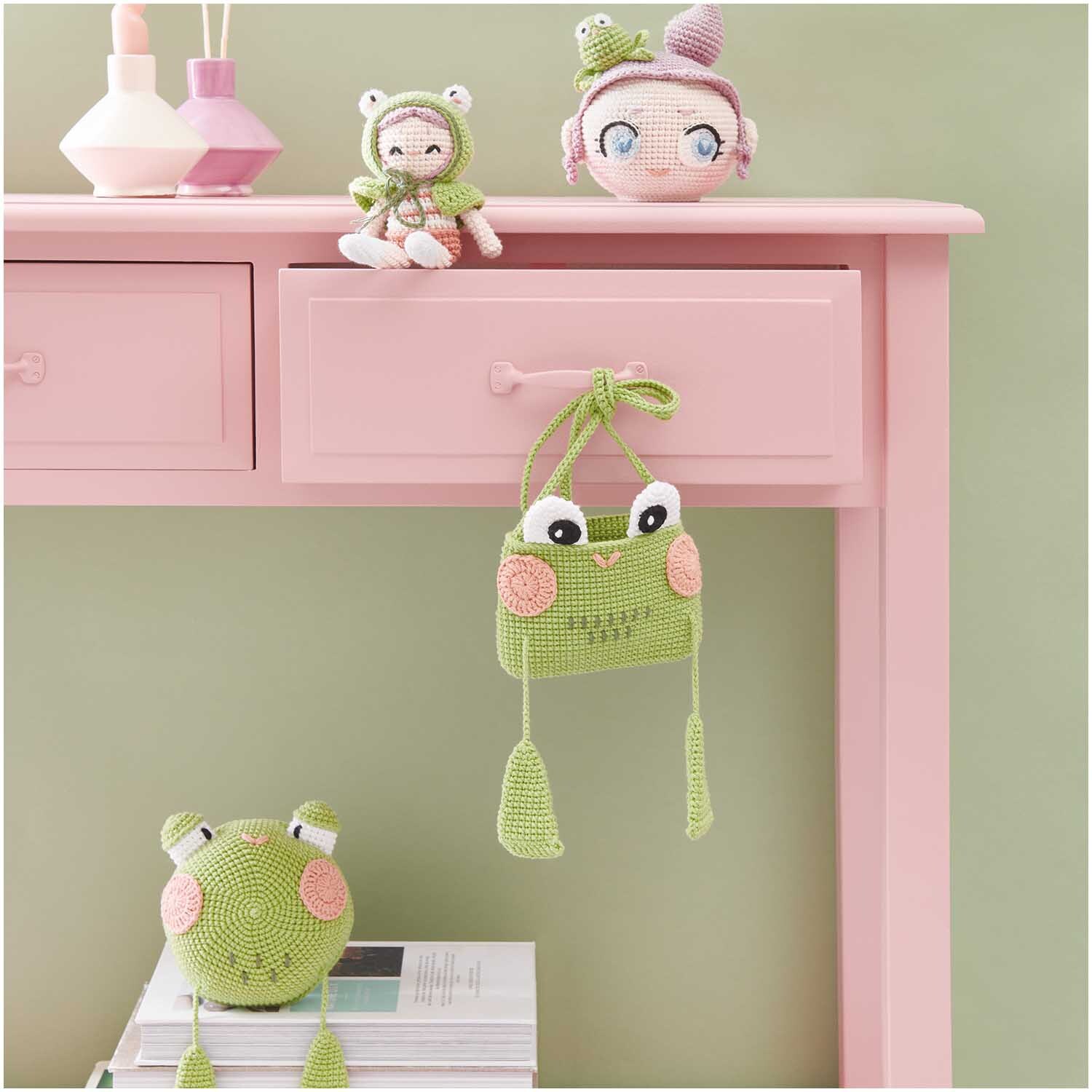 Creative Ricorumi dk: Niedliche grüne Häkeltiere und Accessoires von Rico Design auf rosa Tisch.
