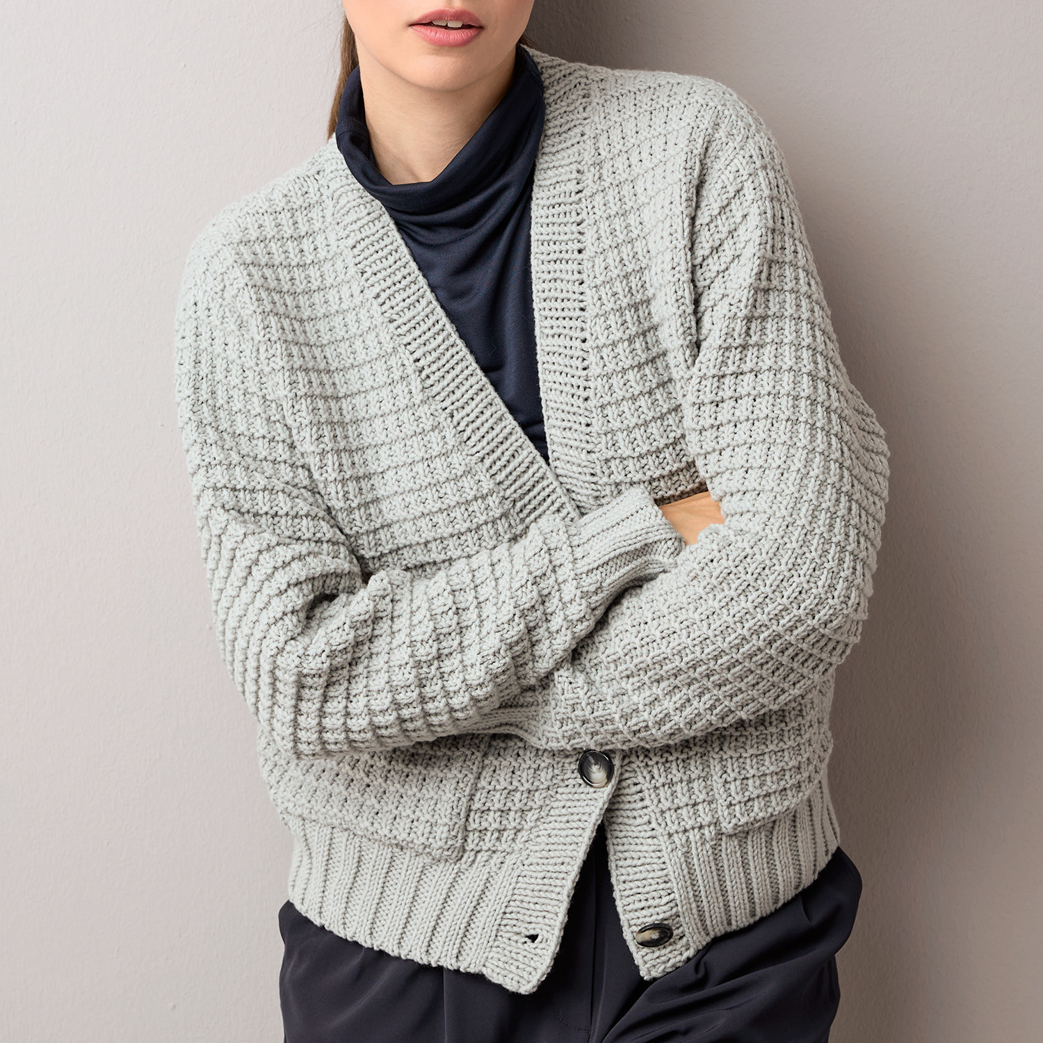 Strickanleitung Cardigan aus Classik: Grauer Cardigan mit Knopfleiste, getragen über schwarzem Oberteil.