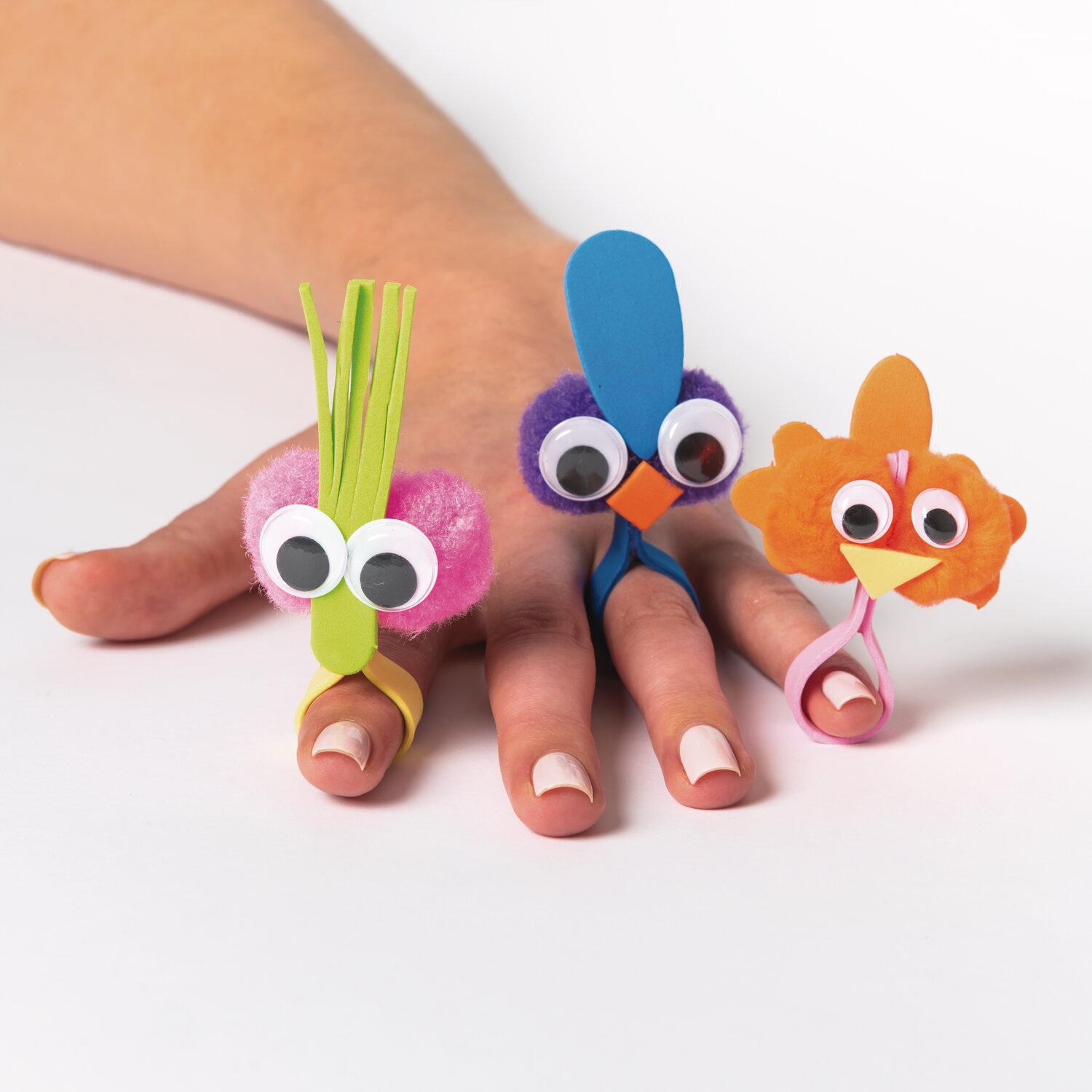 DIY-Bastelset Regenbogen: Drei bunte Fingerpuppen aus Pompons und Papier auf einer Hand.