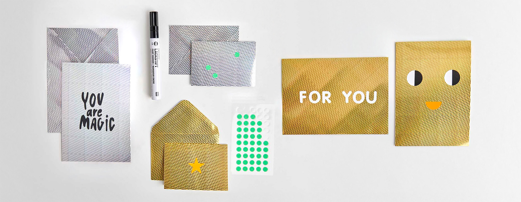 Nebeneinander platzierte silberne, goldene Karten und Umschlag aus Effektpapier, mit Schrift und Stickern gestaltet. Flatlay von Produkten.