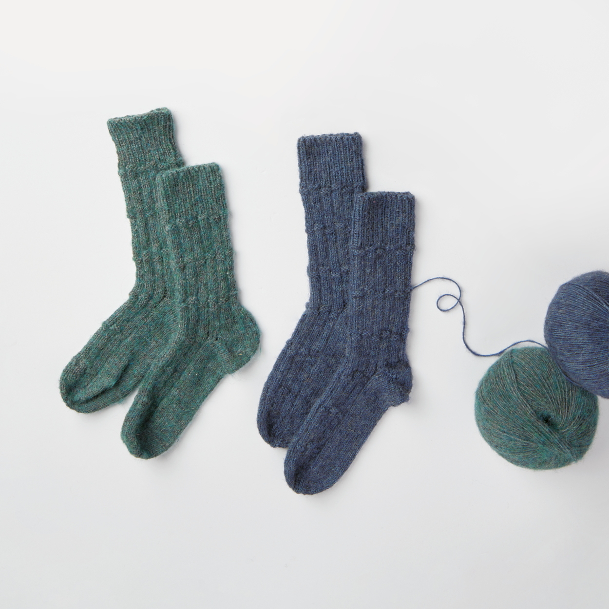 Ein Paar blaue und ein Paar grüne gestrickte Socken mit den dazugehörigen Garnen. Flatlay von Produkten.