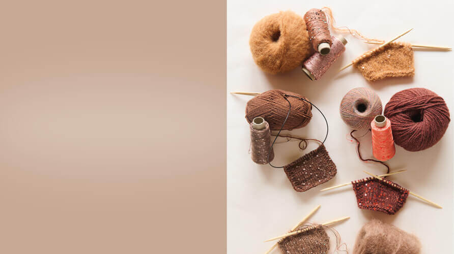 Banner mit Garnen, Strickteilen und Handarbeitszubehör vor beigefarbener Hintergrundfläche