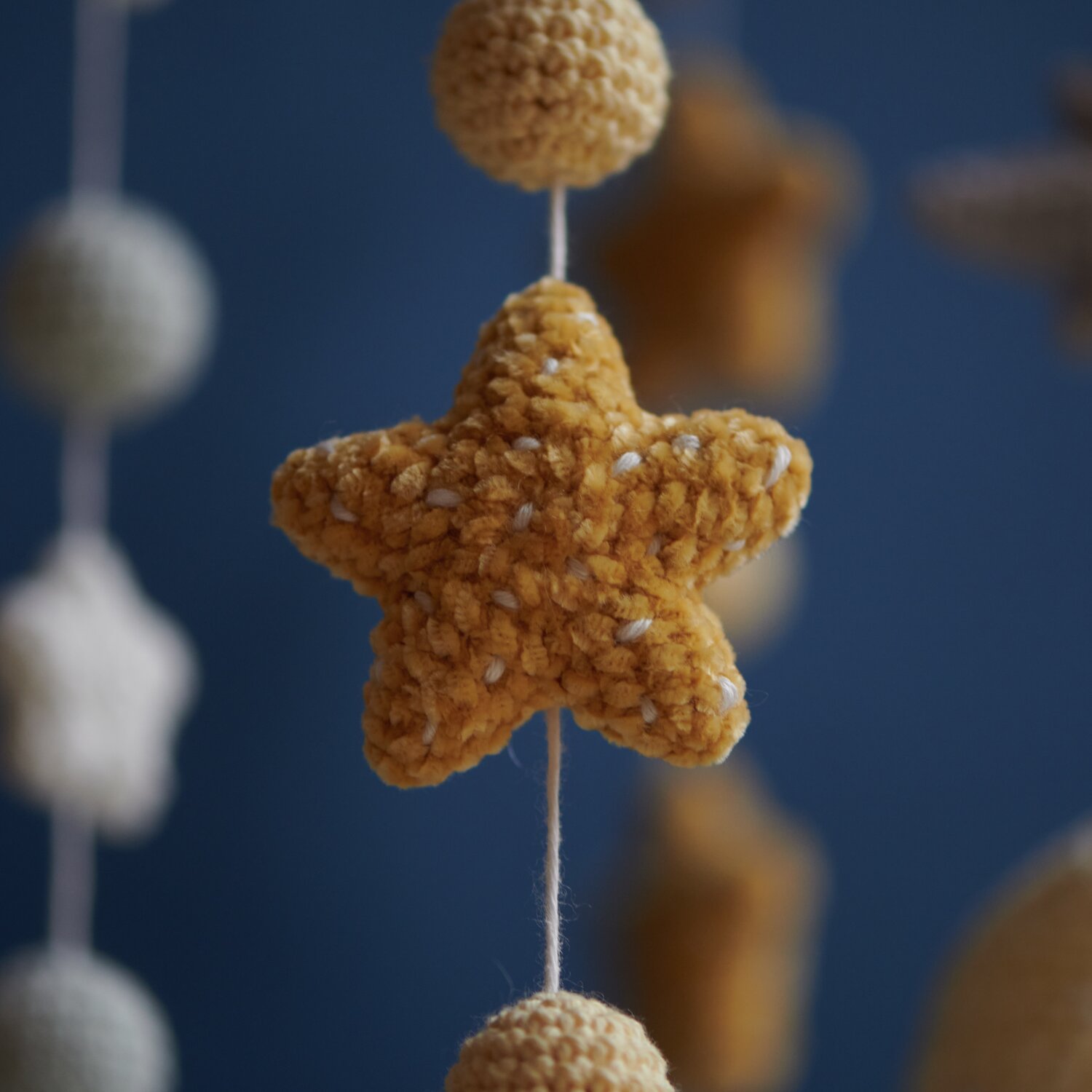 Ricorumi Glow In The Dark: Gehäkelter gelber Stern aus weichem Garn, aufgehängt an einer Schnur vor blauem Hintergrund.