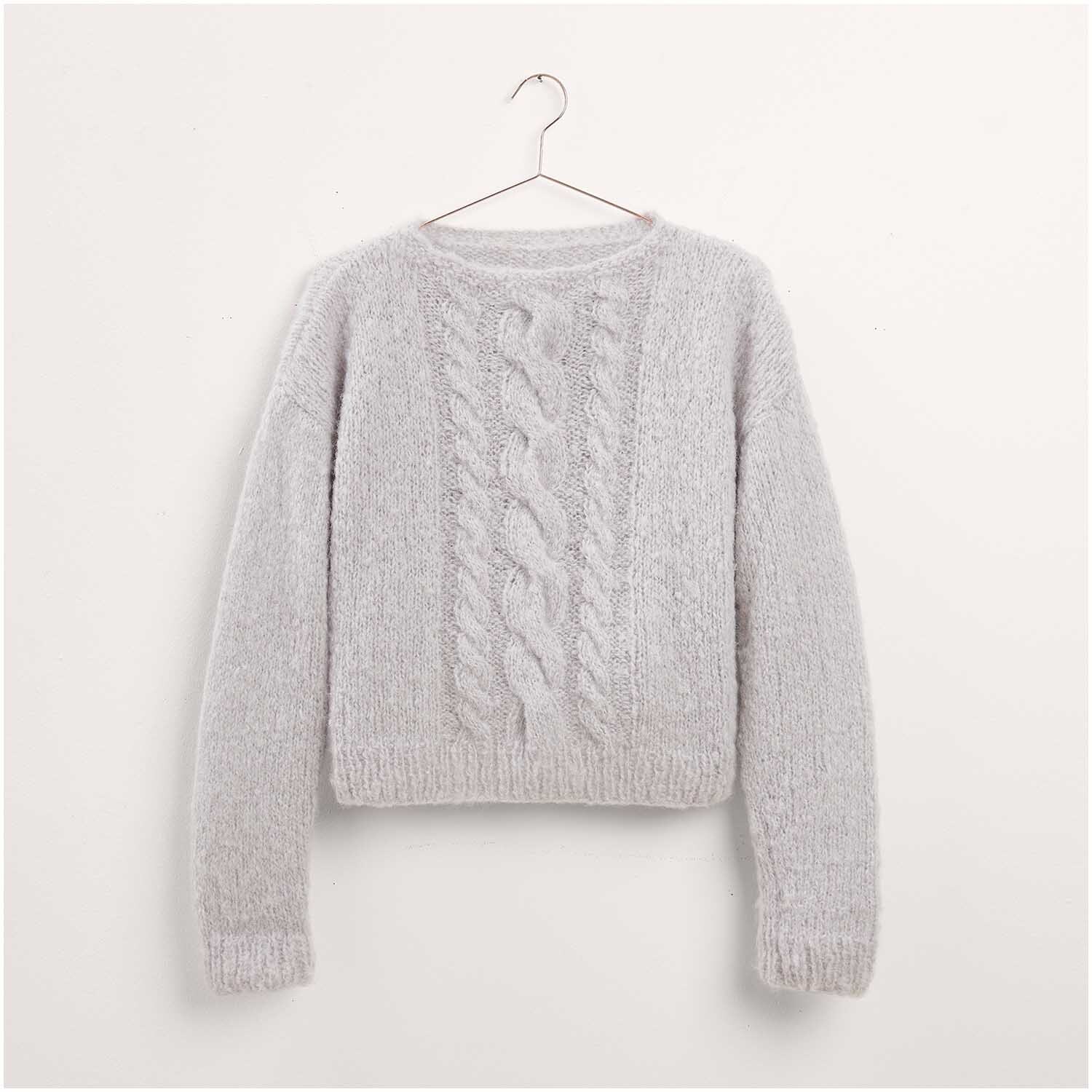 Ein grauer Strickpullover von Made by Me, Modell 37, hängt auf einem Kleiderbügel. Der Pullover zeigt ein Zopfmuster auf der Vorderseite und ist Teil des Stricksets aus Made by Me Nr. 17.