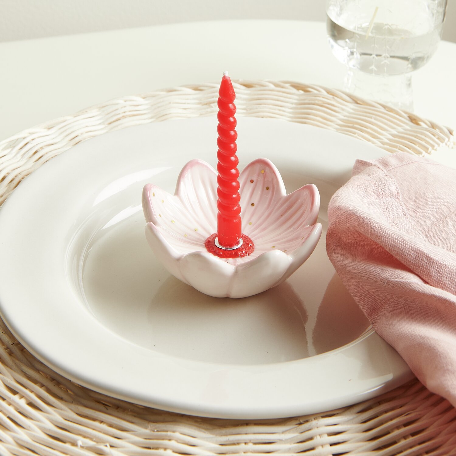 Keramik Kerzenhalter Blüte auf weißem Rattan Deko-Teller mit roter Kerze und rosa Serviette.