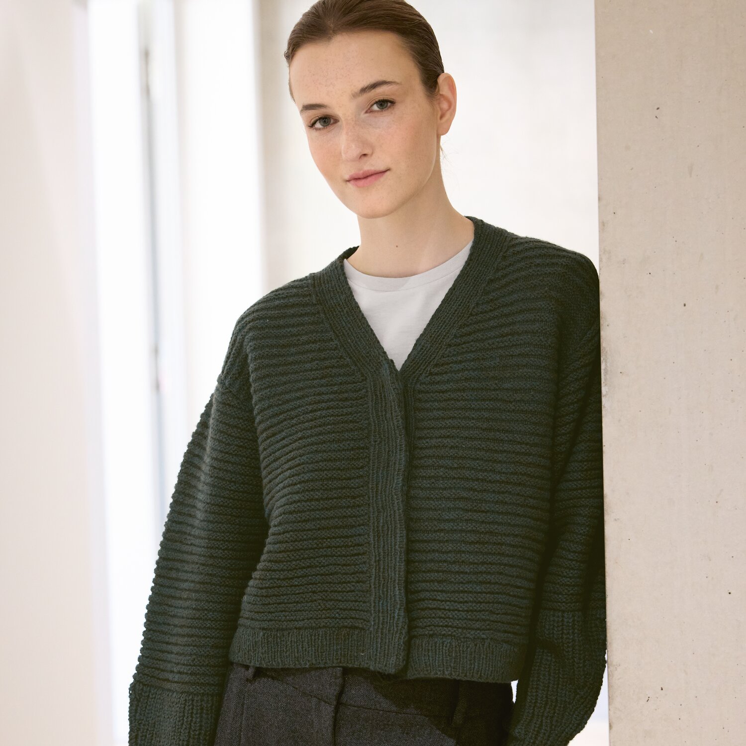 Strickset Jacke Modell 16 aus Luxury Knits - Premium Natural Fibres von Rico Design Strickset Jacke Modell 16 aus Luxury Knits: Dunkelgrüne Strickjacke aus Premium Natural Fibres, getragen von einer Frau vor hellem Hintergrund.