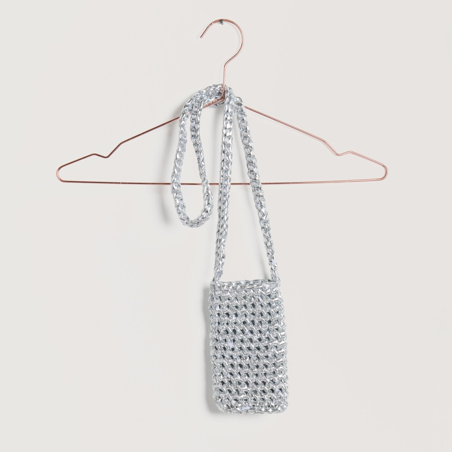 Lovewool No. 22 Frühjahr-Sommer: Silberne, gehäkelte Handytasche aus Creative Leatherette von Rico Design, hängend an einem Kleiderbügel.