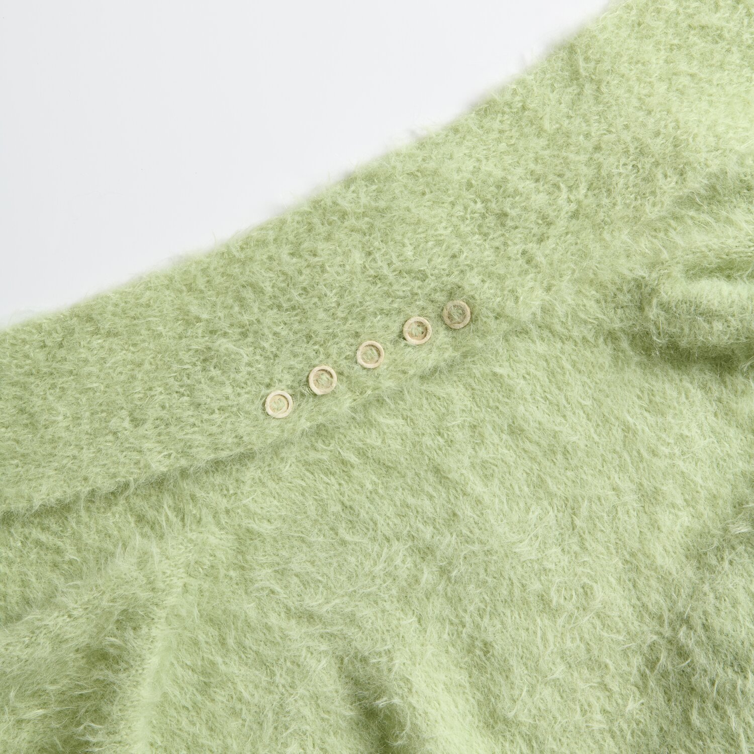 Essentials Super Kid Mohair Loves Silk: Weiches, pistazienfarbenes Strickstück mit Knopfdetails. Ideal für kreative Strickprojekte.