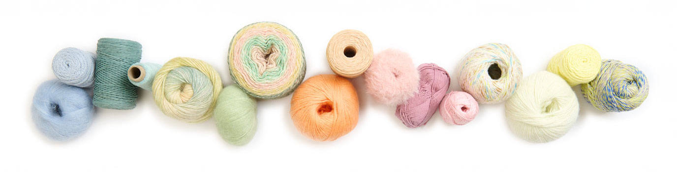Verschiedene Garne farblich sortiert und aneinandergereiht. Flatlay von Produkten.