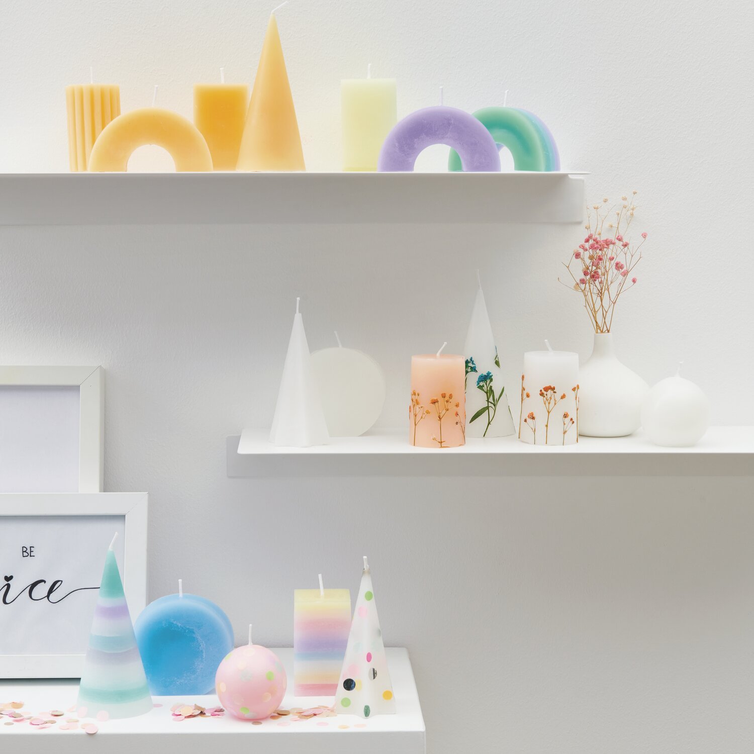Kerzenwachs Pastillen: Bunte, geometrische Kerzen auf weißen Regalen, dekoriert mit Trockenblumen.