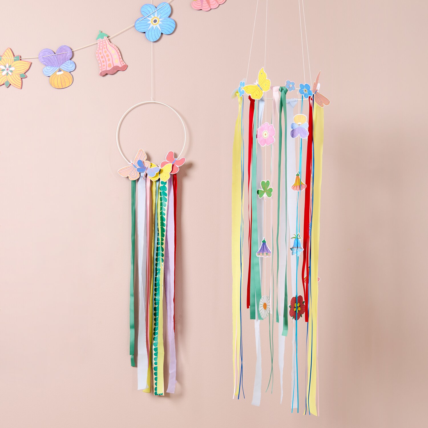 Bastelpapierblock Midsommar Magic mit 23 Blatt von Rico Design, gezeigt als farbenfrohe Papiergirlanden und Hängedekoration mit langen Bändern an rosafarbener Wand