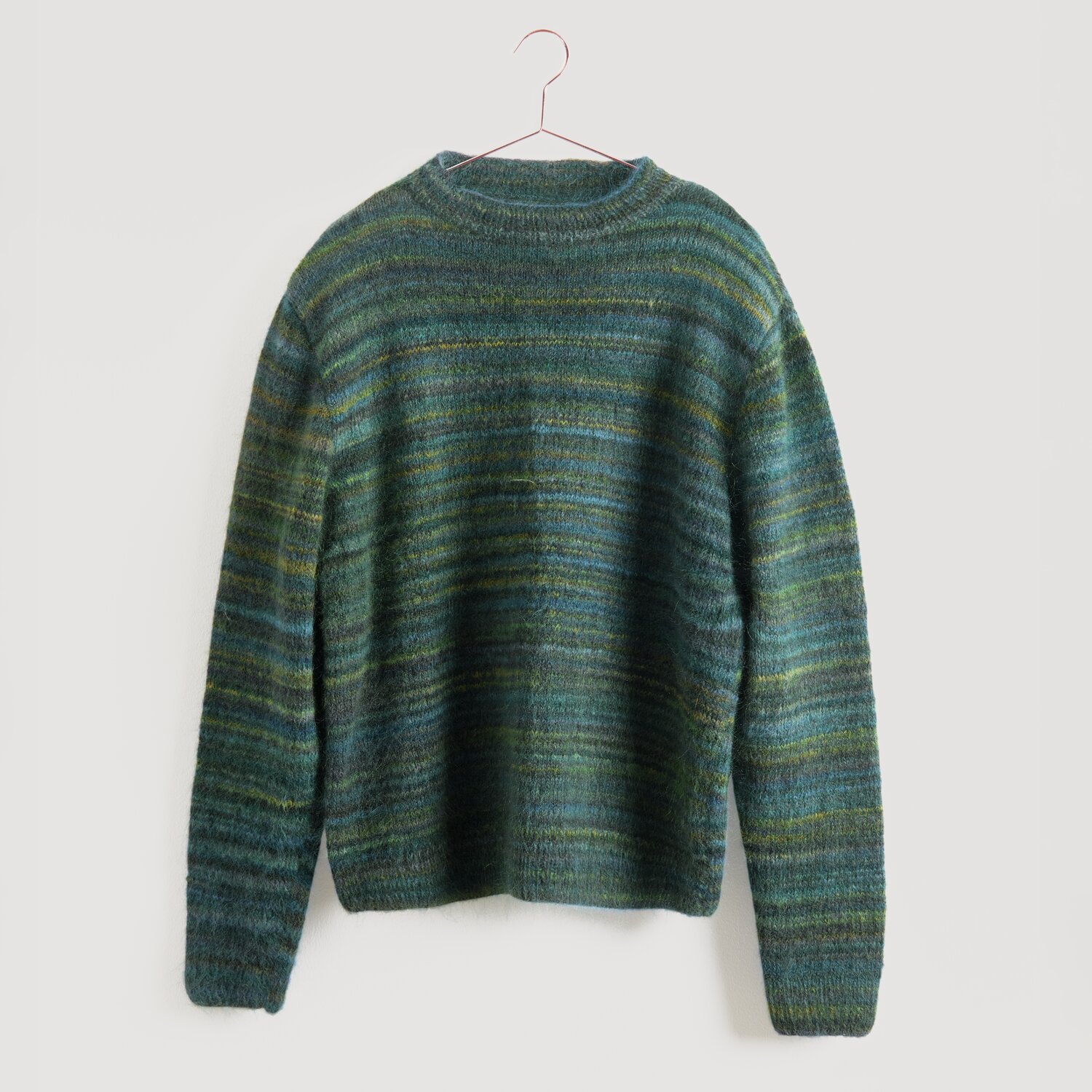 Lovewool No. 21 Herbst-Winter Sprachauswahl deutsch von Rico Design Grüner gestreifter Pullover von Modell Legeware, hängend an einem Kleiderbügel. Der Pullover hat horizontale Streifen in verschiedenen Grüntönen und ist ideal für kühle Tage.
