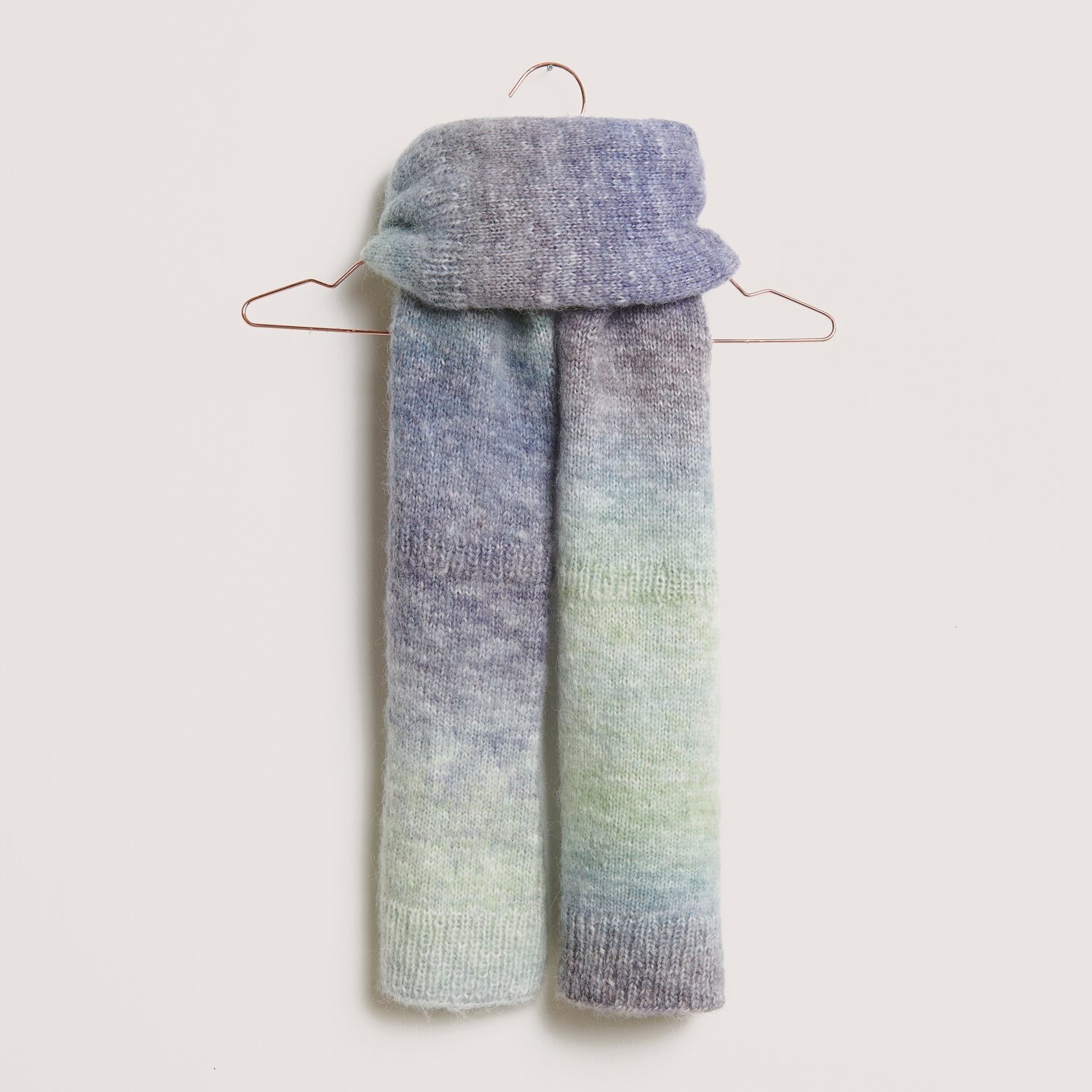 Die Neue Masche No. 14 Winter von idee. Creativmarkt Creative Painted Power Schal in sanften Blau- und Grüntönen, aufgehängt an einem Kleiderbügel.