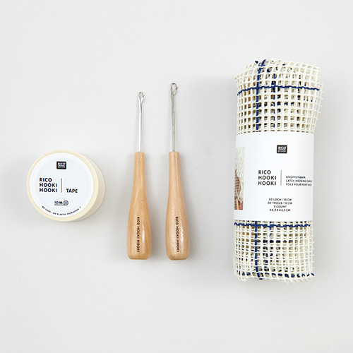 Ein Tape in der Verpackung, zwei Knüpfhaken und einmal verpacktes Knüpfstramin. Flatlay von Produkten.